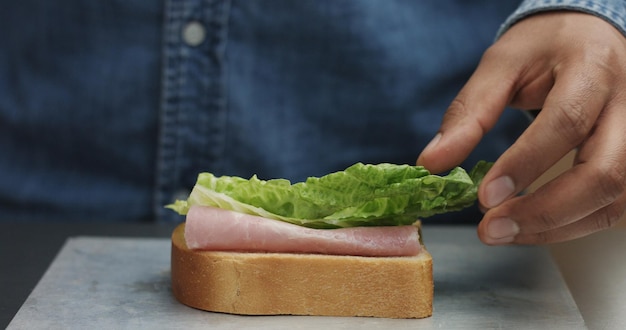 Closeup of man's hand making sandwich puts from sides all ingredients on plate