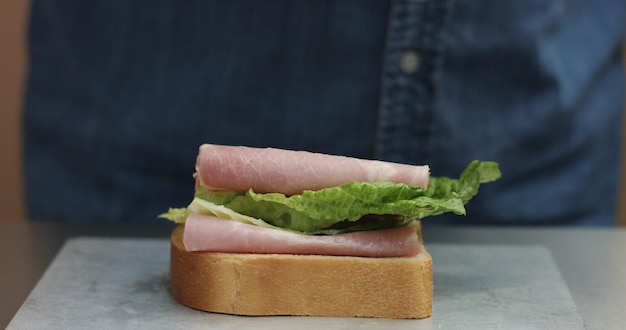 Free photo closeup of man's hand making sandwich puts from sides all ingredients on plate