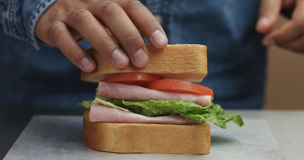 Free Photo closeup of man's hand making sandwich puts from sides all ingredients on plate