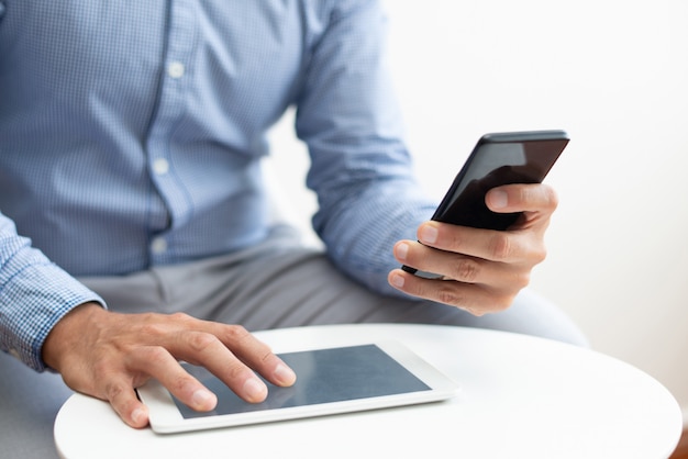 Free Photo closeup of man using smartphone and tablet at coffee table