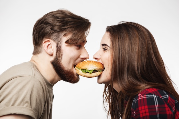 Closeup of man and woman eating one burger together.