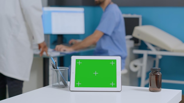 Free photo closeup of mock up green screen chroma key tablet computer with isolated display standing on desk in hospital office. multiethnic medical team analyzing sickness report working at healthcare treatment