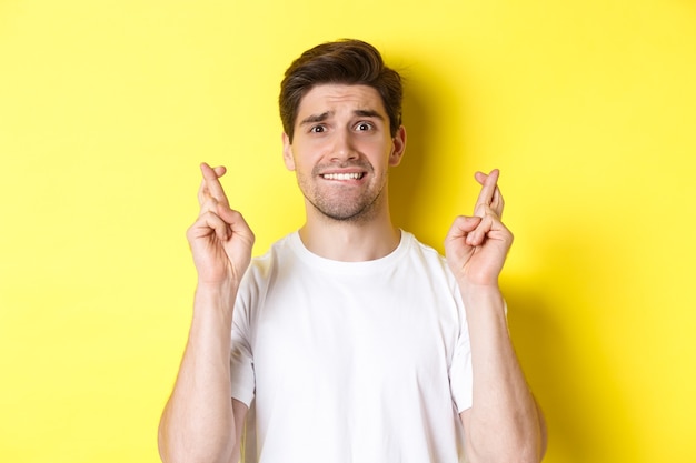 Free Photo closeup of nervous man making wish holding fingers crossed and biting lip worried standing over yell...