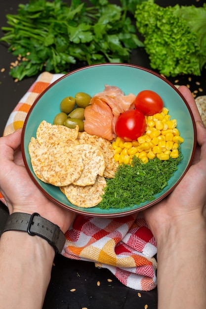 Free photo closeup of a person holding a bowl of salad with salmon, crackers and vegetables under the lights