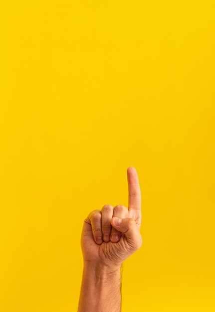 Closeup of a person pointing up isolated on a yellow background with space for text