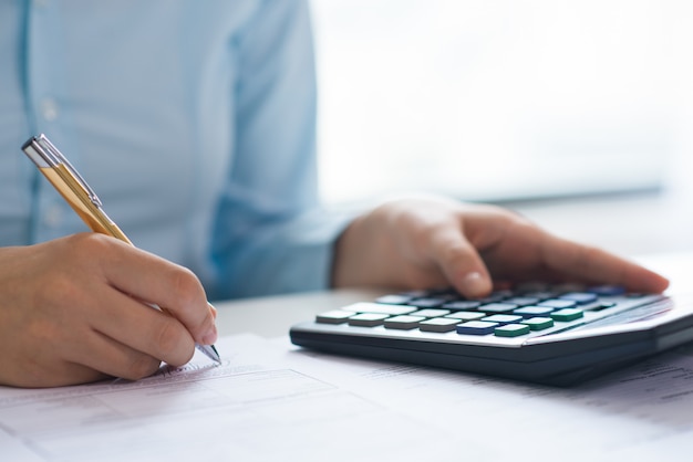 Free photo closeup of person signing document and using calculator