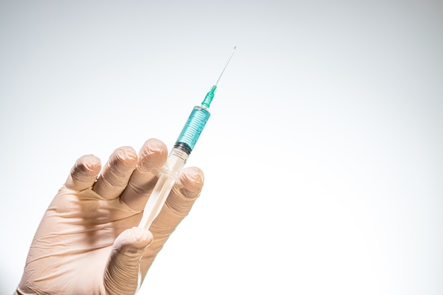 Closeup of a person with a latex glove holding a needle syringe isolated on white