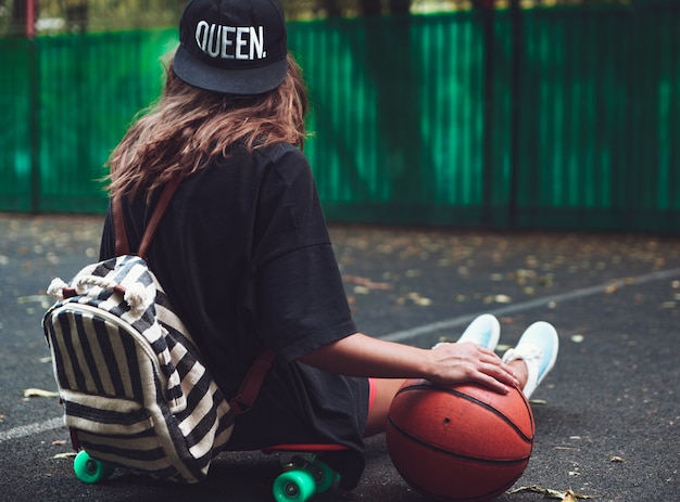 Free Photo closeup photo basketball ball with girl sitting on plastic orange penny shortboard on asphalt