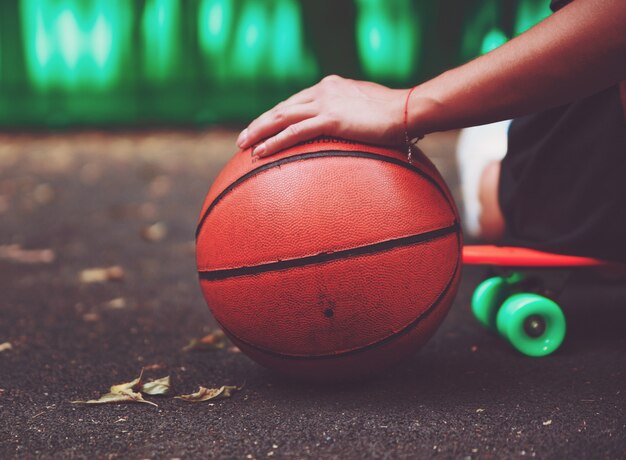 Closeup photo basketball ball with girl sitting on plastic orange penny shortboard on asphalt