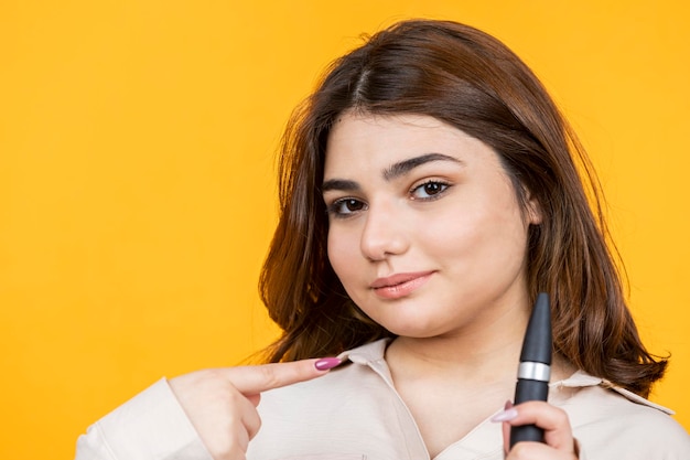 Closeup photo of young lady holding mascara and point finger on it High quality photo