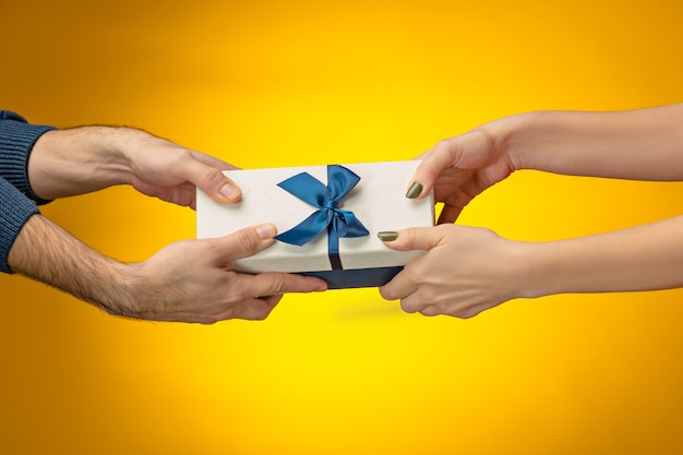 closeup picture of man and woman's hands with gift box on yellow background