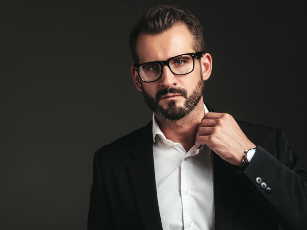 Closeup portrait of handsome confident stylish hipster lambersexual model Sexy modern man dressed in elegant black suit Fashion male posing in studio on dark background In spectacles