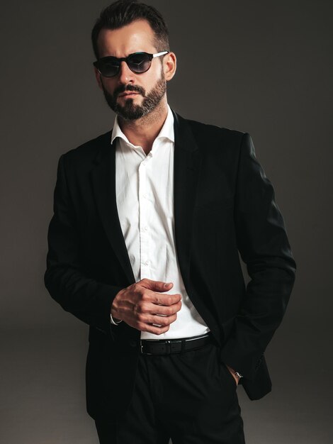 Closeup portrait of handsome confident stylish hipster lambersexual model Sexy modern man dressed in elegant black suit Fashion male posing in studio on dark background In sunglasses