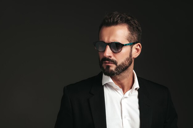 Closeup portrait of handsome confident stylish hipster lambersexual model Sexy modern man dressed in elegant black suit Fashion male posing in studio on dark background In sunglasses