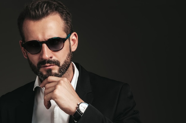 Free photo closeup portrait of handsome confident stylish hipster lambersexual model sexy modern man dressed in elegant black suit fashion male posing in studio on dark background in sunglasses