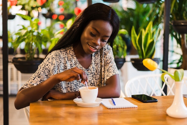 Closeup portrait of happy young black woman drinking coffee in cafe