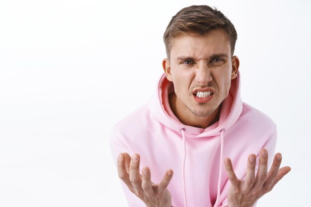 Closeup portrait of hateful annoyed and bothered blond man arguing swearing and cursing person feel upset over failure shaking hands and grimacing aggressive standing white background