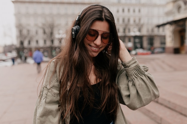 Closeup portrait of joyful smiling woman relaxing with music in the city Outdoor shot of smiling female model in headphones spending time on the weekend