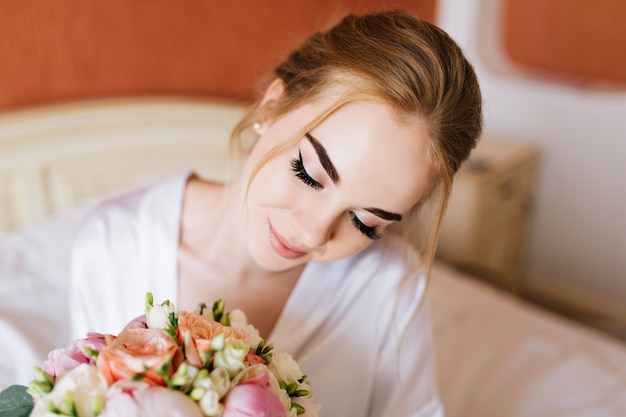 Free Photo closeup portrait pretty happy bride in white bathrobe in the morning in appartment. she looks  at bouquet of flowers  in hands and smiling