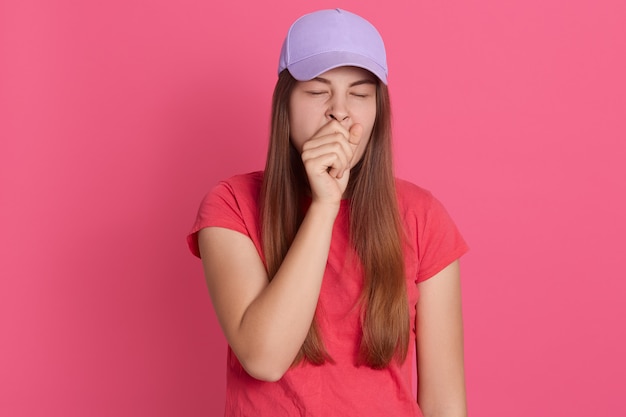 Free photo closeup portrait of tired yawning woman covering her mouth with fist, looks exhausted, wearing t shirt and baseball cap,