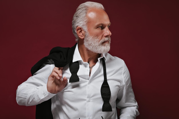 Closeup portrait of white haired man in shirt Stylish bearded guy with tattoos in light shirt looking away on burgundy background