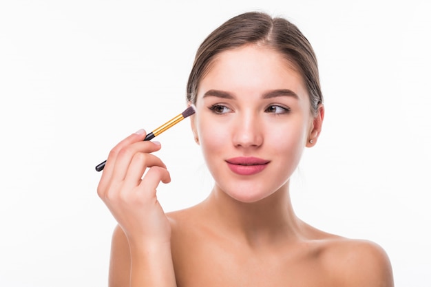 Closeup portrait of a woman applying dry cosmetic tonal foundation on the face using makeup brush isolated on white wall