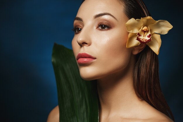 Closeup portrait of woman with slicked back hair, tender lily flower behind ear. Looking away. Beauty concept.