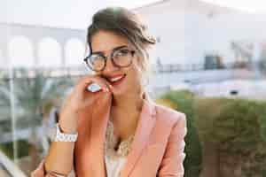 Free photo closeup portrait of young gorgeous girl in stylish glasses, pretty student, business woman wearing elegent pink jacket, beige blouse with lace, day makeup. big window  with view on yard.