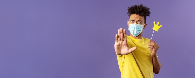 Closeup portrait of young hipster guy in medical mask stretch hand forward stop gesture holding smal