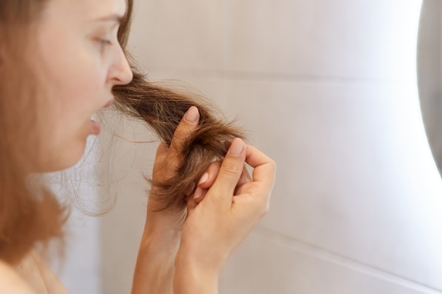 Free Photo closeup profile portrait of upset astonished woman looking at her dry hair, having problems, needs to change shampoo or special treatment at trichological clinic.