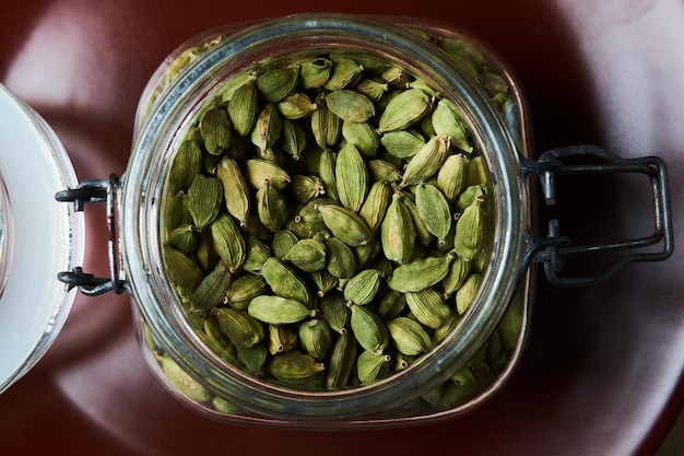 Free Photo closeup proto of glass jar full of green cardamom pods on brown plate. top view.