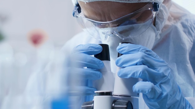 Closeup of scientist doctor looking into medical microscope analyzing blood sample during scientific experiment in biochemistry laboratory. Researcher man developing vaccine against covid19