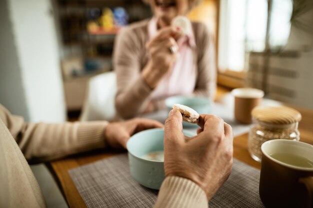 Closeup of senior man eating cookie while having breakfast with his wife at home