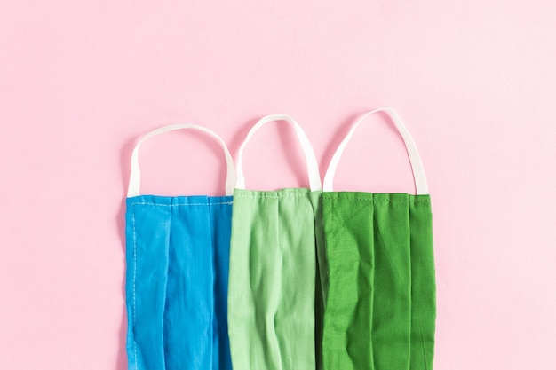 Closeup shot of blue, light green, and dark green protective face masks on a pink background