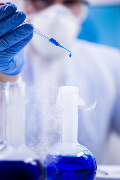 Closeup shot of blue solution dropping from a pipette used by a scientist in a research laboratory.