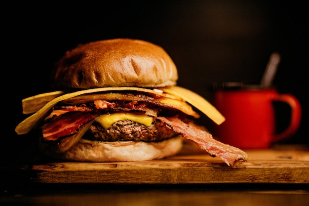 Closeup shot of a burger with bacon and cheese, a red coffee mug