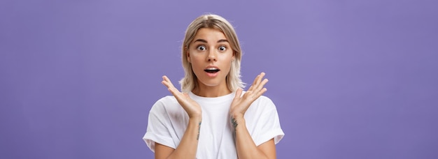 Free photo closeup shot of charmed and impressed goodlooking caucasian girlfriend with blond hair and tattoos on arms raising hands in amazed and excited gesture opening mouth and gazing mesmerized at camera