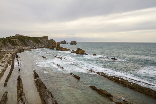 Closeup shot of a cliffy seashore near a wavy sea under a cloudy sky