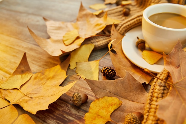 Closeup shot of a cup of coffee and autumn leaves on wooden surface