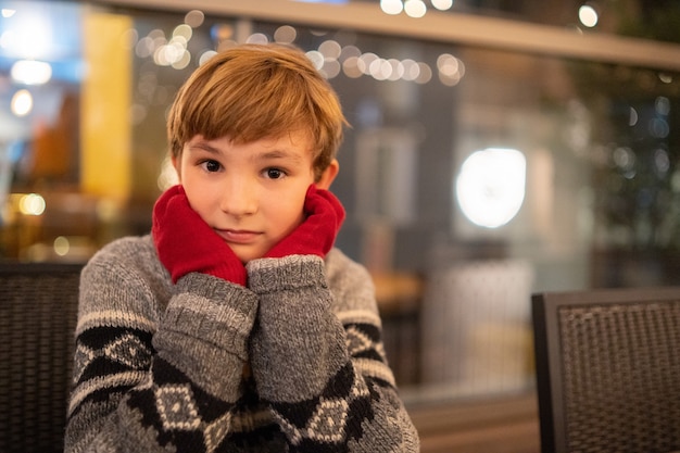 Free Photo closeup shot of a cute blond boy sitting with the hands in red gloves on the cheeks