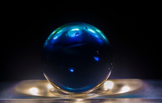 Closeup shot of a dark blue marble on top of a lit surface with a dark background