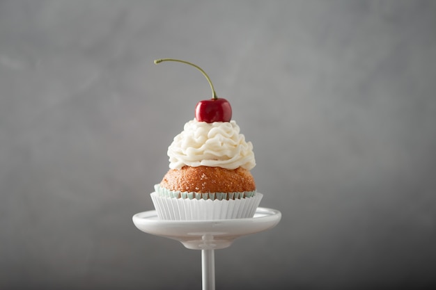 Free photo closeup shot of a delicious cupcake with cream and cherry on top on a dessert stand