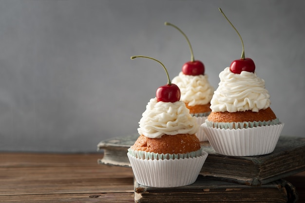 Free Photo closeup shot of delicious cupcakes with cream and cherry on top on books