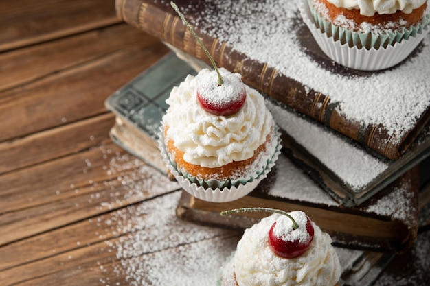 Closeup shot of delicious cupcakes with cream, powdered sugar, and a cherry on top on books