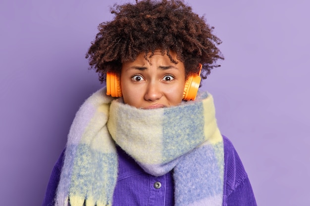 Free photo closeup shot of displeased african american female shivers from cold wears warm scarf around neck spends much time outside during winter time listens audio track via headphones.