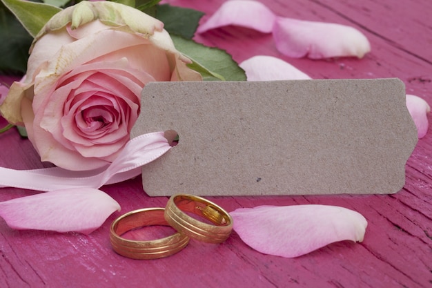 Free photo closeup shot of engagement rings, a tag and beautiful pink roses on the table