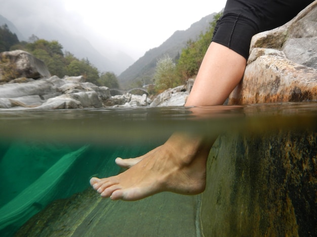 Closeup shot of feet underwater in a river with mountains in Ticino, Switzerland.