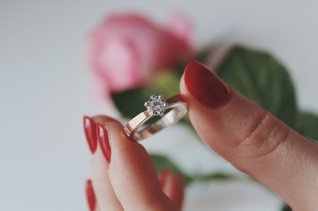 Free photo closeup shot of a female holding a gold diamond ring with a pink rose