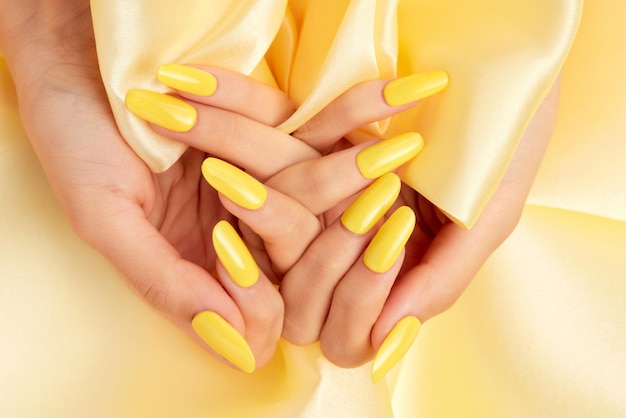 Closeup shot of a female's hands with yellow nail polish on a yellow silk fabric