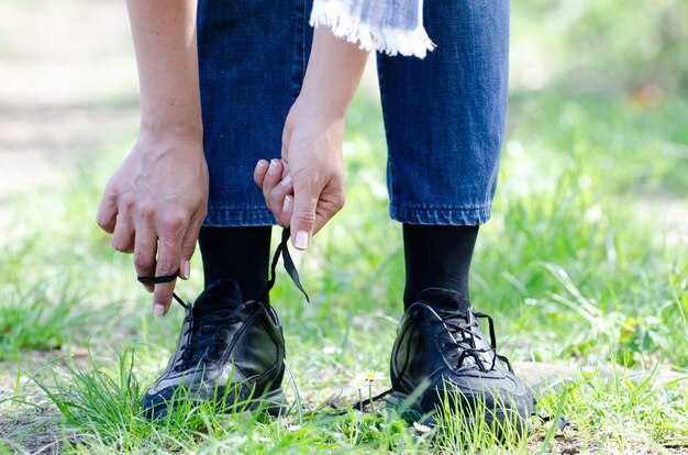 Closeup shot of a female tying her shoelaces on a path with grass